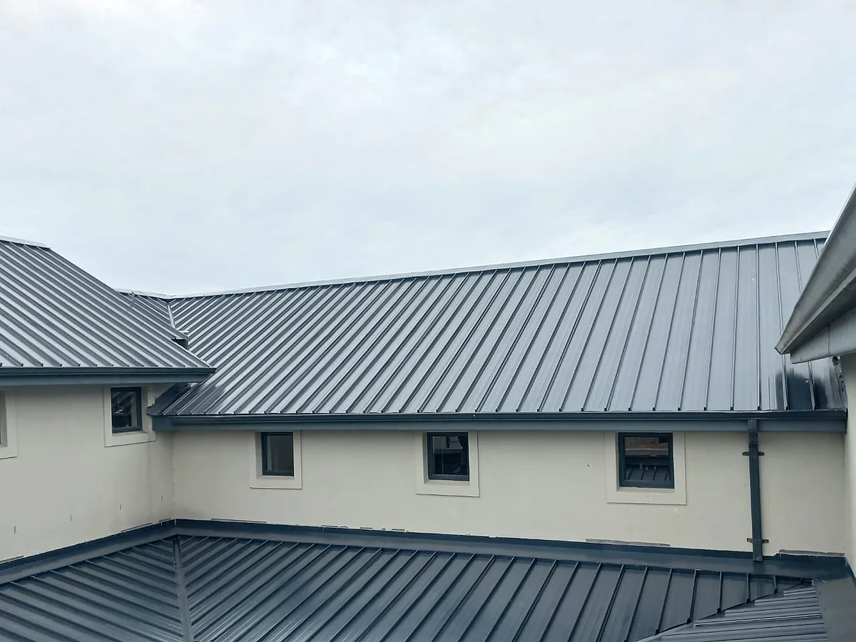 New grey metal roof around a courtyard, with hips, valleys and new gutters against the white walls of a double-storey home