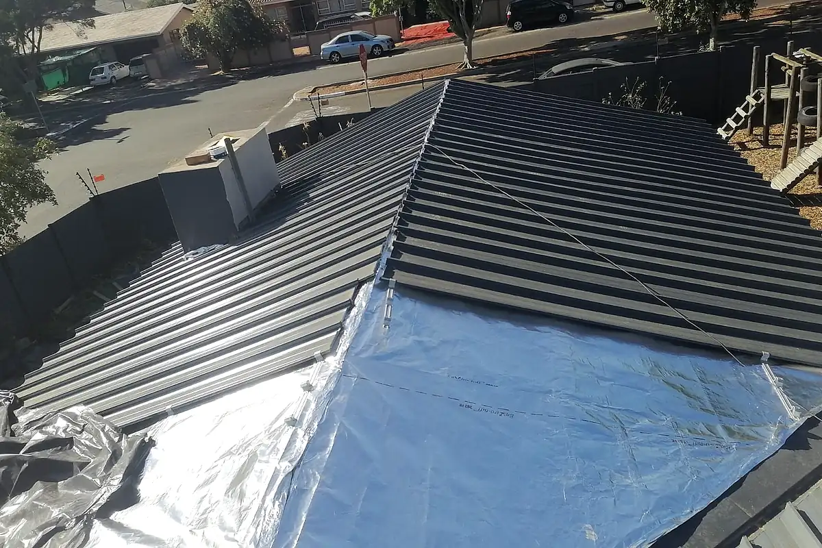 New dark metal roof sheeting being fixed over a silver reflective foil underlay on a house