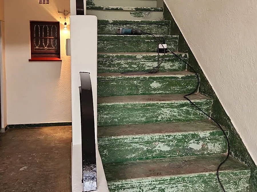 Worn staircase at Morlea Court with old green paint peeling off the steps, before the work