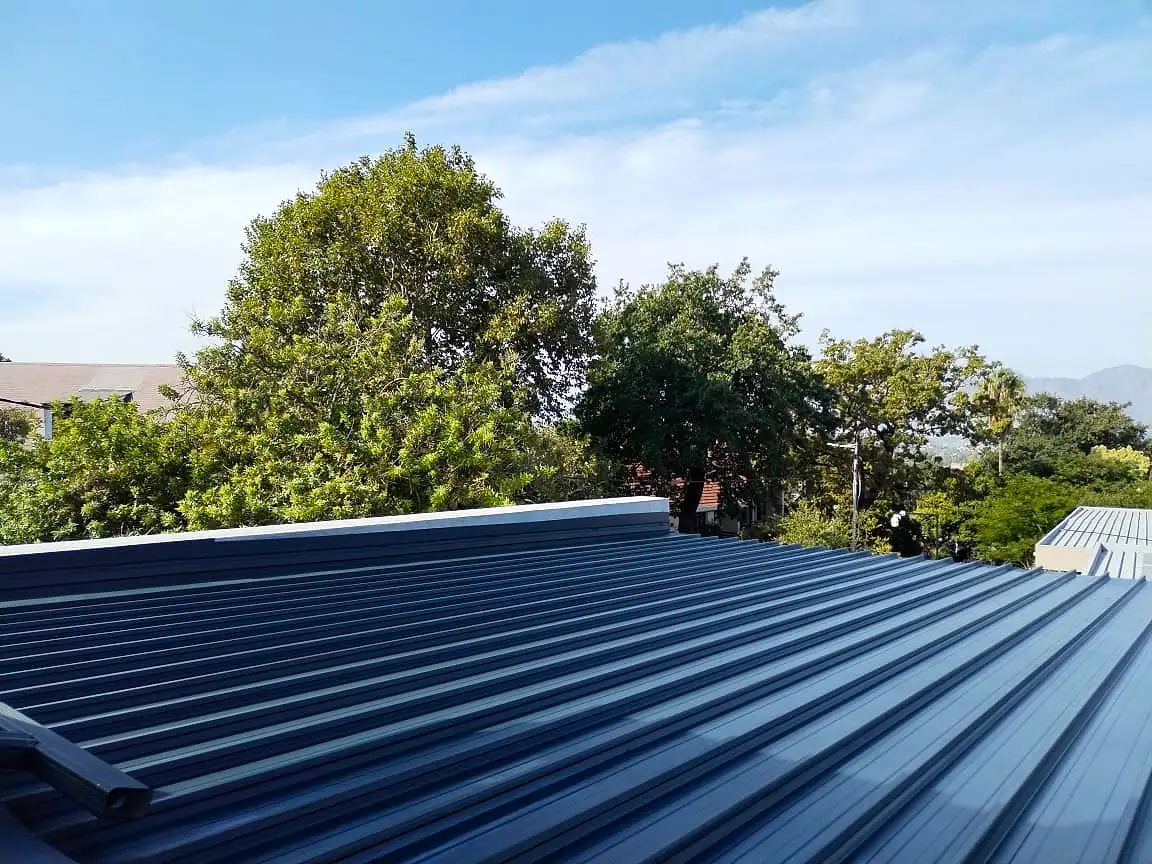 New dark blue metal roof sheeting on a house, with trees and blue sky behind