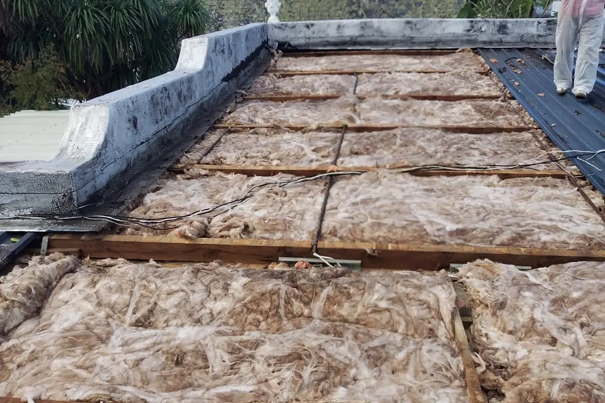 An opened-up roof showing old, discoloured insulation between the timbers next to a parapet wall
