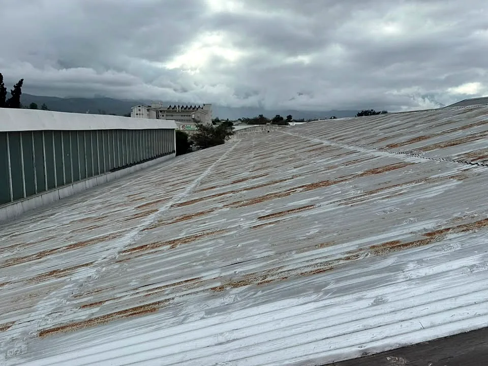 Rust streaks along a large corrugated metal roof on a commercial building, before painting